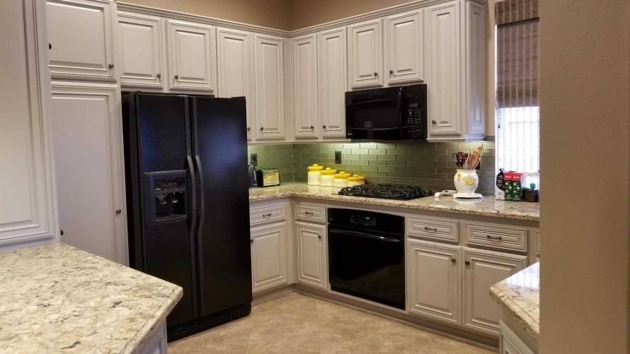 A kitchen with white cabinets , a black refrigerator , a stove , and a microwave.