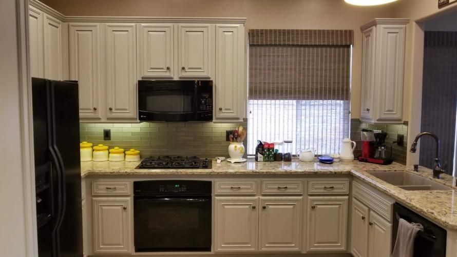A kitchen with white cabinets , a black refrigerator , a stove , a microwave , and a sink.