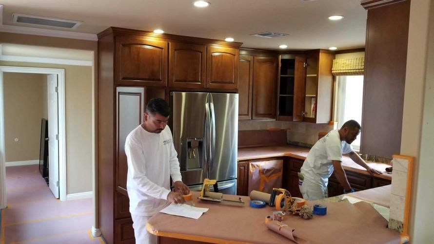 Two men are painting a kitchen in a house.