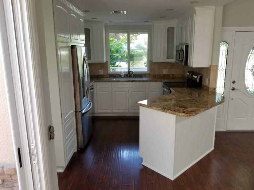 A kitchen with white cabinets , granite counter tops , stainless steel appliances and hardwood floors.