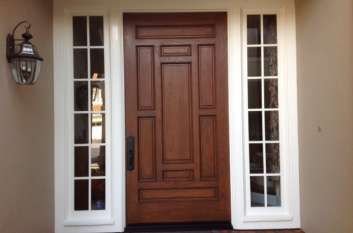 A brown wooden door with white trim and windows on a house.
