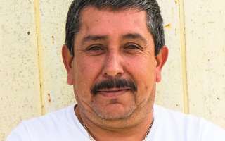 A man with a mustache is wearing a white shirt and smiling.