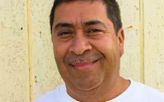 A man with a mustache is smiling and wearing a white shirt.