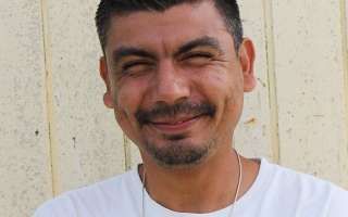 A man with a beard and mustache is wearing a white shirt and smiling.