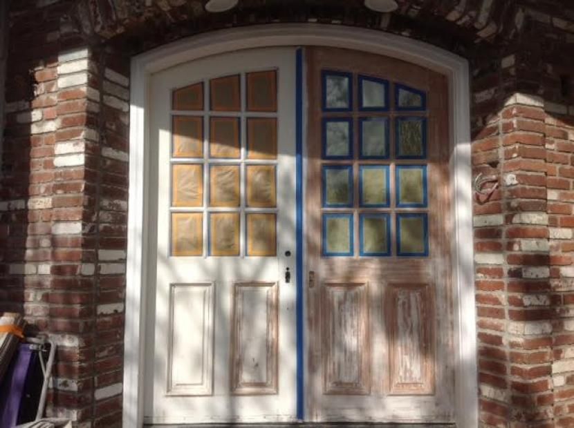 A door is being painted in front of a brick building.