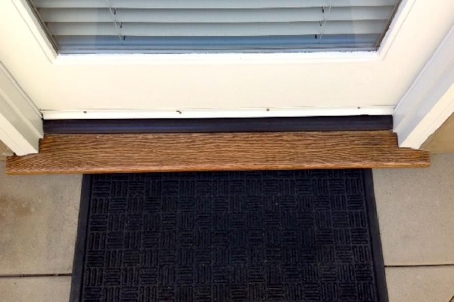 A door with a wooden sill and a black mat underneath it.