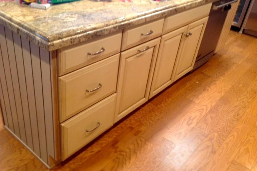 A kitchen island with white cabinets and drawers and a granite counter top.