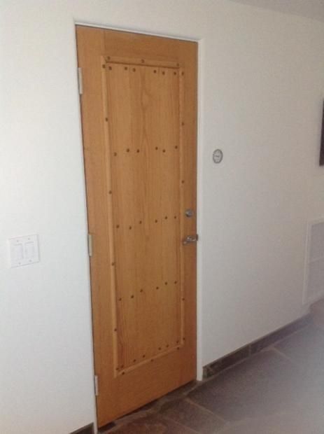 A wooden door is in a hallway next to a white wall.
