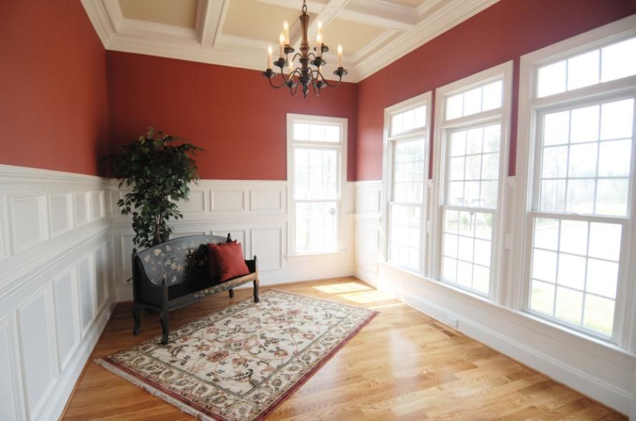A living room with red walls , white trim , hardwood floors and a chandelier.