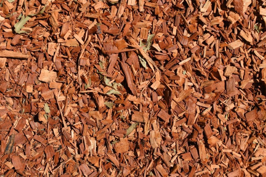 Reddish-Brown Wood Chips on The Ground, Covering a Garden Bed — Cessnock Landscaping Supplies In Cessnock, NSW