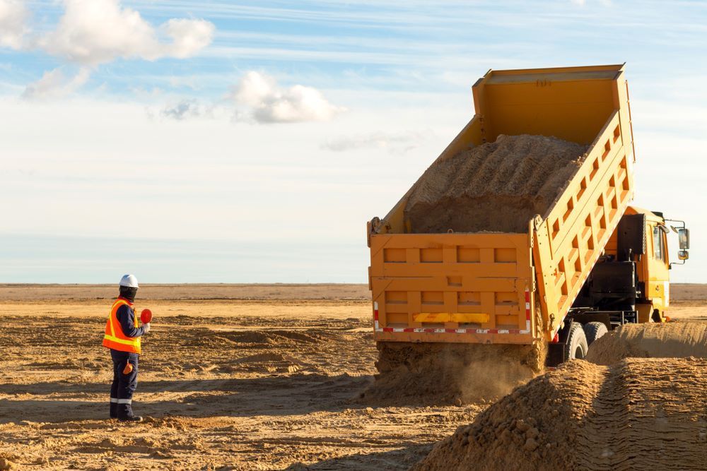 Construction Worker Watches a Yellow Dump Truck Unloading Dirt — Cessnock Landscaping Supplies In North Rothbury, NSW