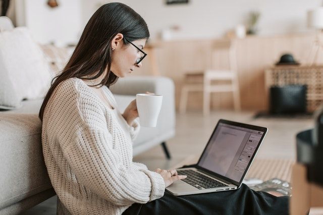 A woman is sitting on a couch using a laptop computer while holding a cup of coffee.