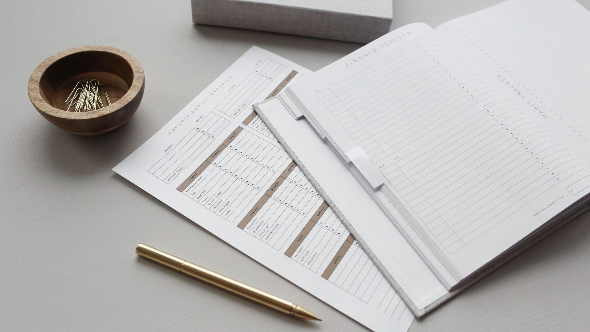 A stack of papers with a pencil and a bowl of pins on a table.