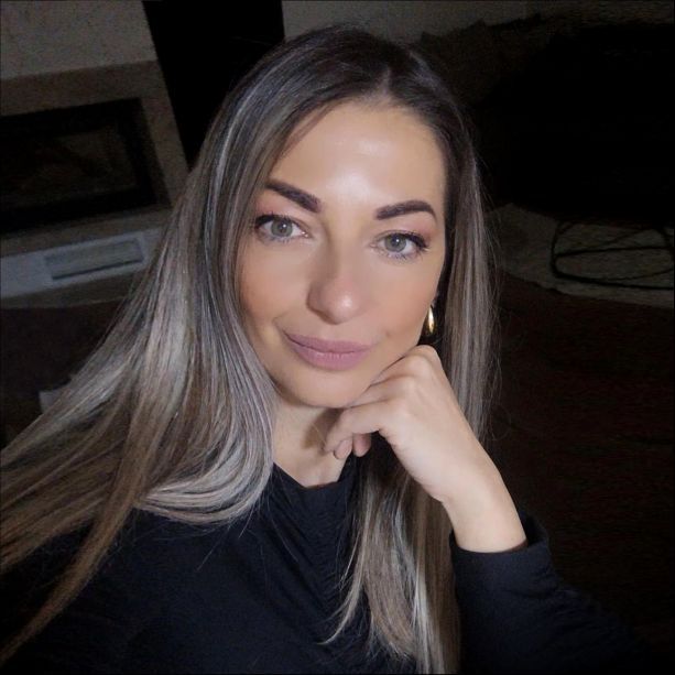 A man wearing a plaid shirt and a black t-shirt is standing with his hands in his pockets.