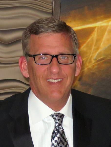 A man wearing glasses and a suit and tie is smiling.