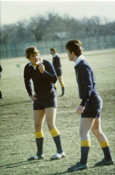 Two men in shorts are standing on a field talking to each other