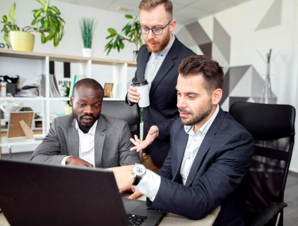 Three men are looking at a laptop computer in an office.