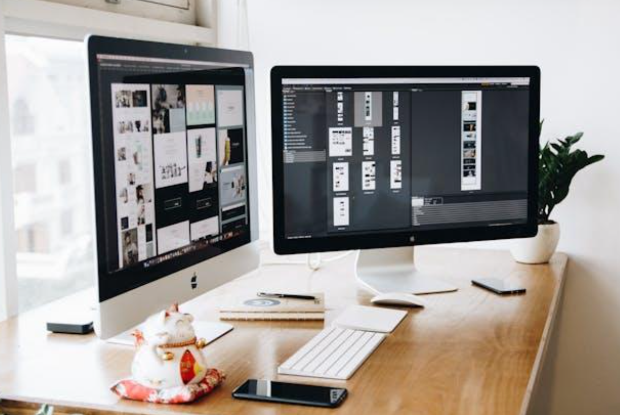 Two computer monitors are sitting on a wooden desk.