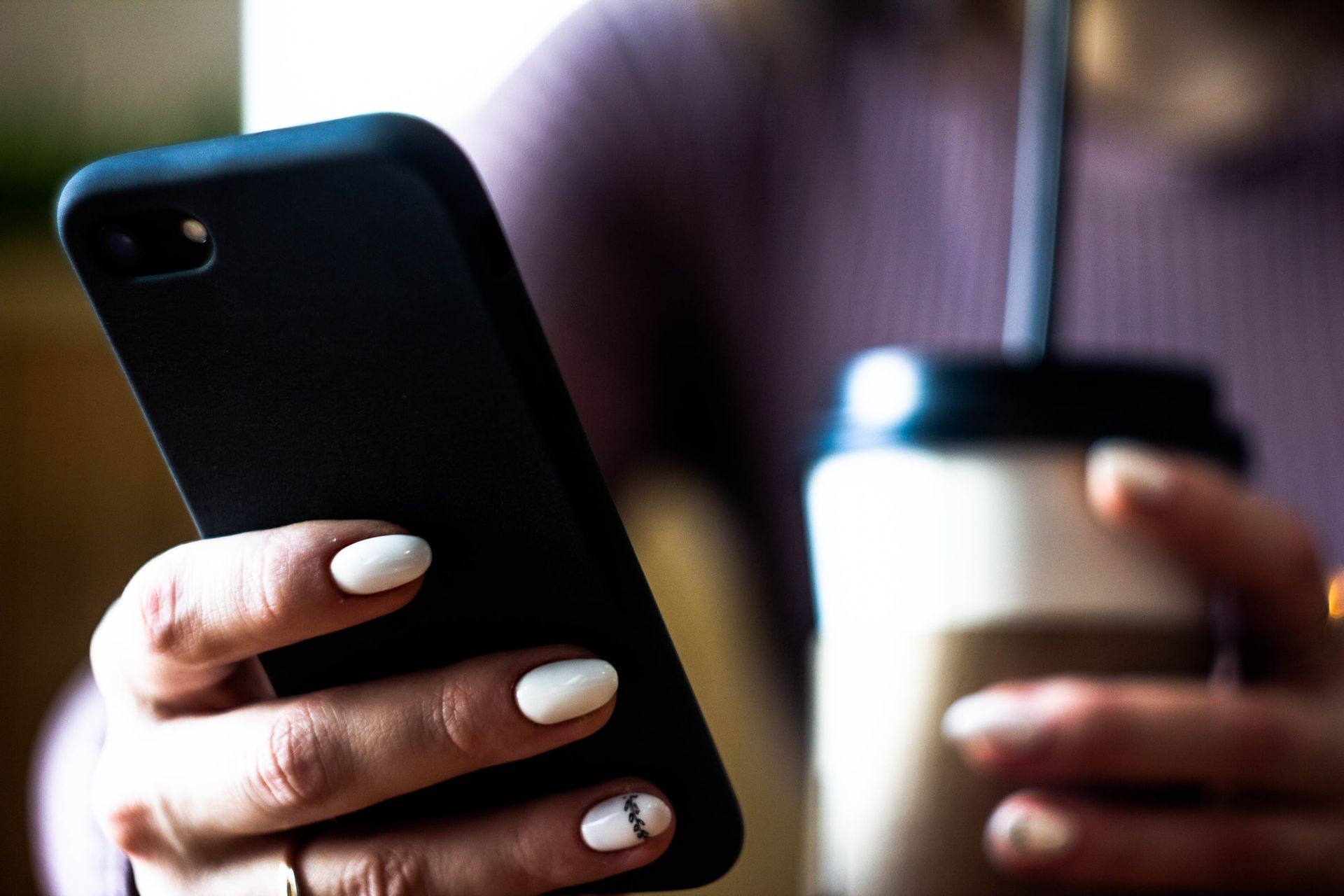 A woman is holding a cup of coffee and a cell phone.