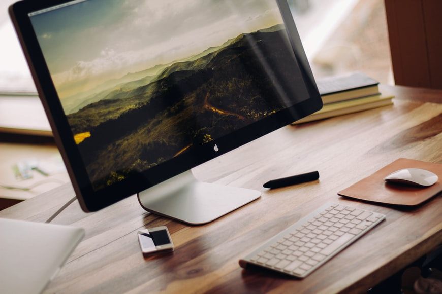 A computer monitor is sitting on a wooden desk next to a keyboard and mouse.