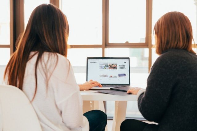 Two women are sitting at a table using a laptop computer.