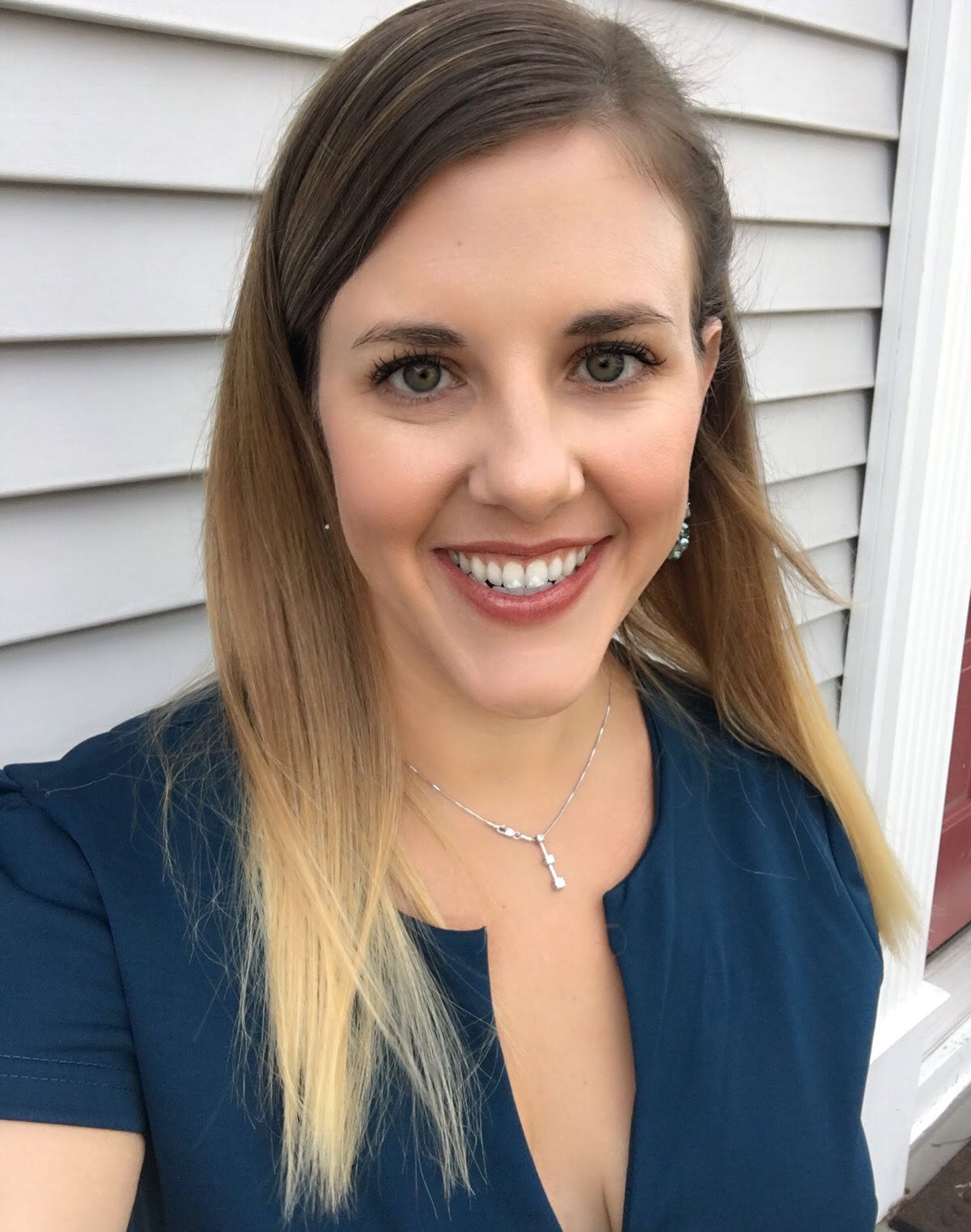 A woman wearing a blue shirt and a necklace is smiling for the camera.