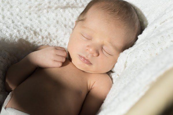 A newborn baby is sleeping on a white blanket.