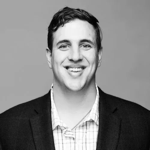 A man in a suit and plaid shirt is smiling in a black and white photo.