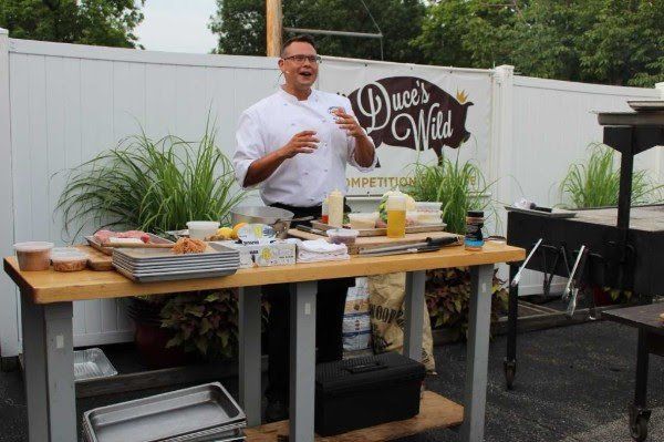 A man is standing in front of a wooden table with food on it.