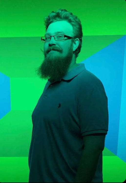 A man with a beard and glasses is standing in front of a green and blue background.