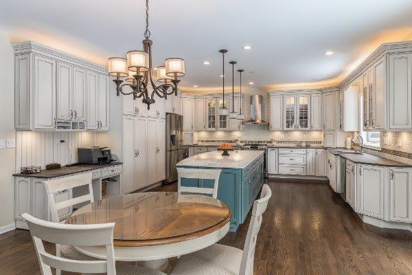 A kitchen with white cabinets , a table and chairs , and a chandelier.