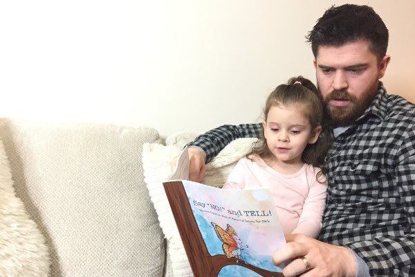 A man is reading a book to a little girl on a couch.