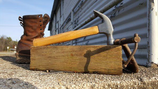 A hammer is sitting on a wooden box next to a pair of boots.