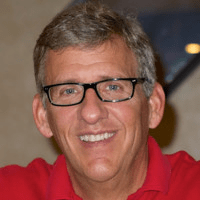 A man wearing glasses and a red shirt is smiling for the camera.