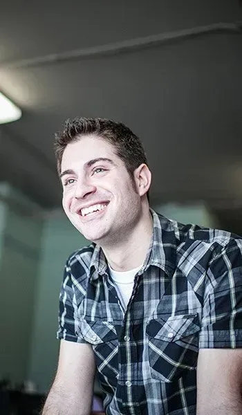 The man is wearing a plaid shirt and smiling.