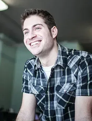 The man is wearing a plaid shirt and smiling.