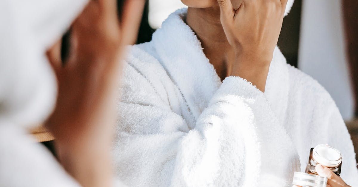 A woman in a bathrobe is looking at her face in a mirror.