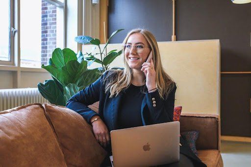 A woman is sitting on a couch with a laptop and talking on a cell phone.