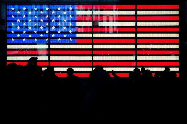 A group of people are standing in front of a large american flag.