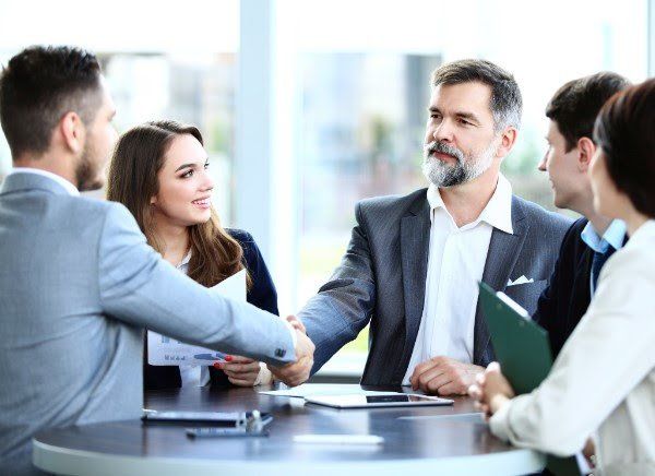 A group of people are sitting around a table shaking hands.