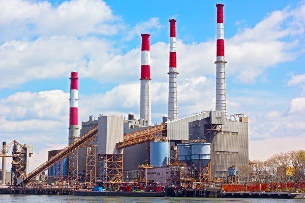 A large power plant with red and white chimneys next to a body of water.