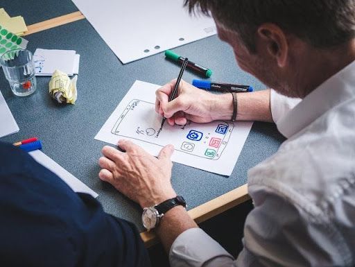 A man and a woman are sitting at a table drawing on a piece of paper.