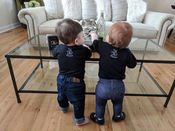 Two babies standing next to each other on a glass coffee table