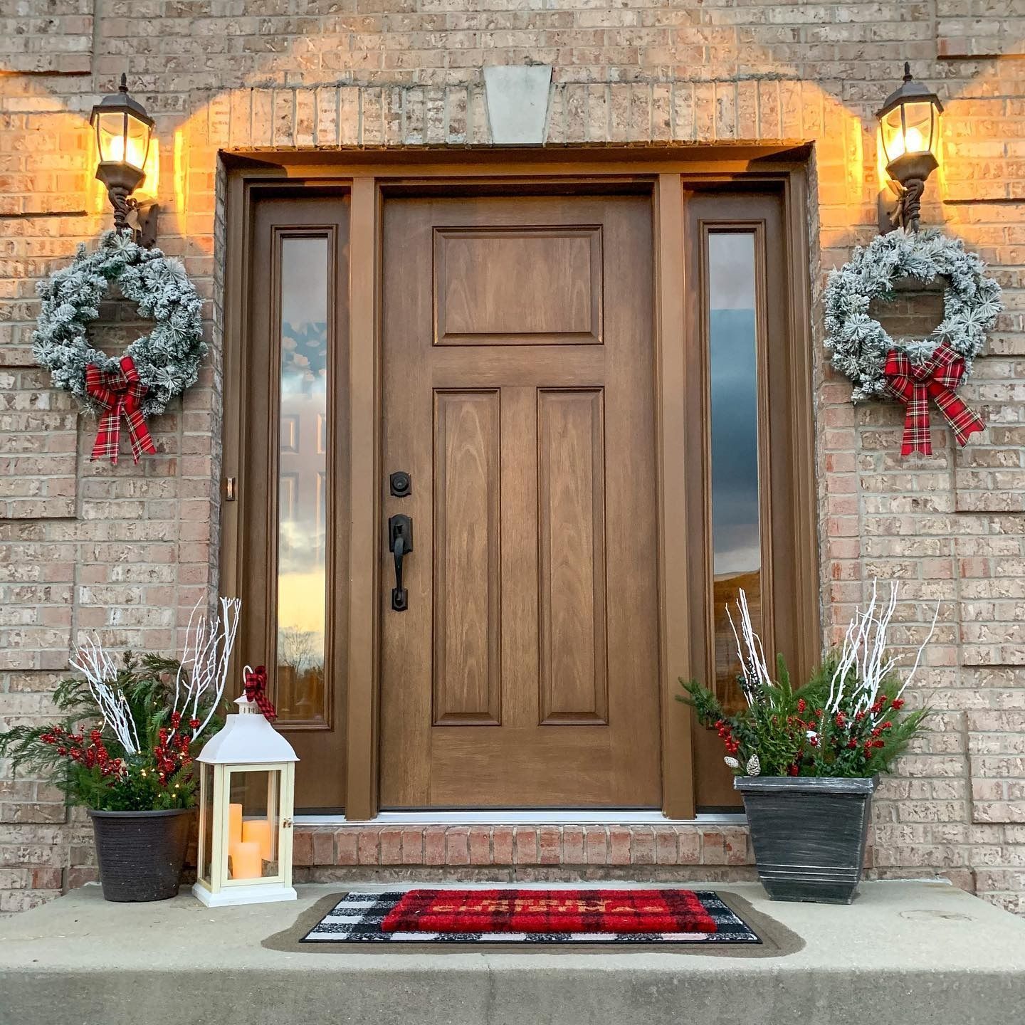 Wooden front door decorated with wreaths, lights, and planters for the holidays.