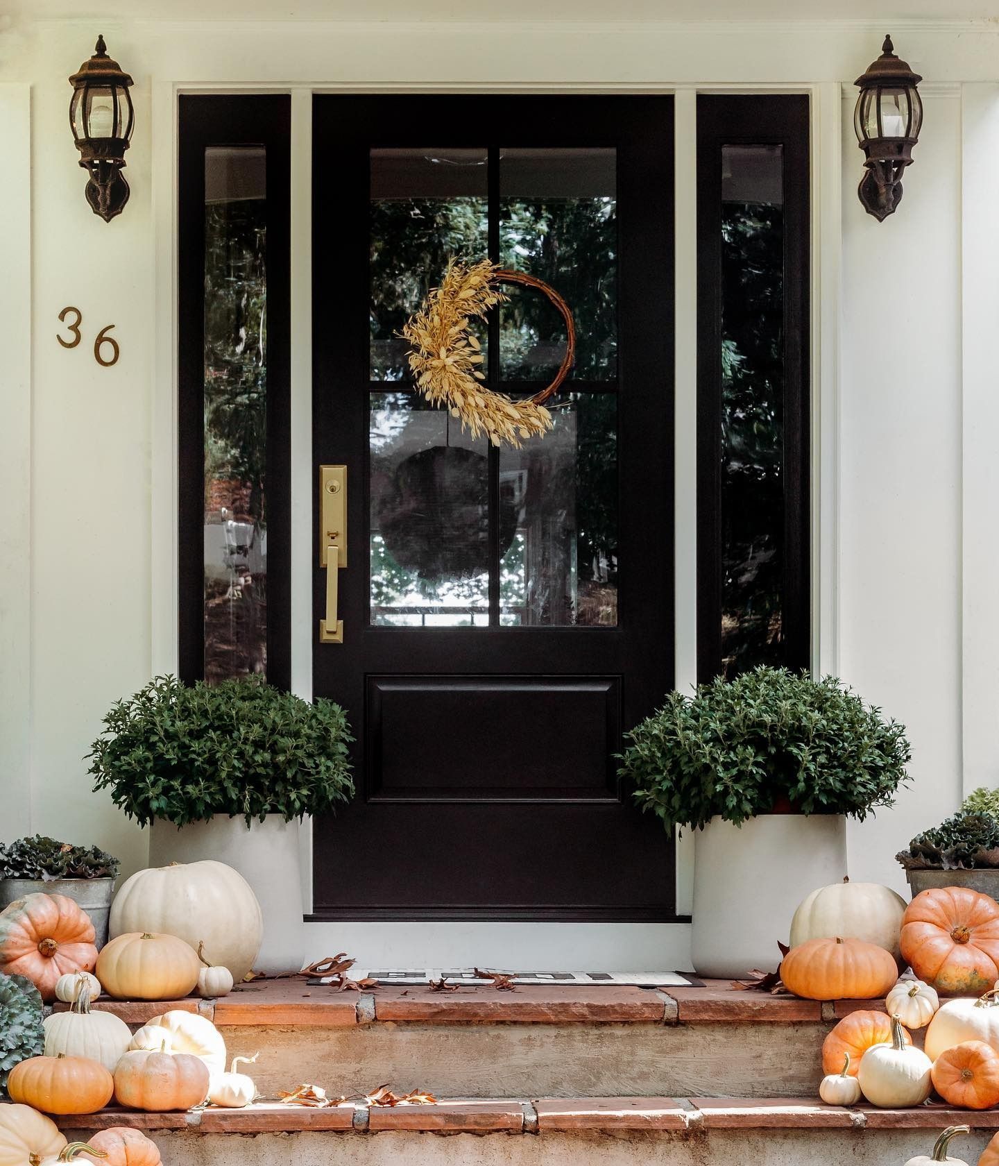 Fall-decorated front porch with pumpkins, wreath, and potted greenery. Black door with sidelights, address number 