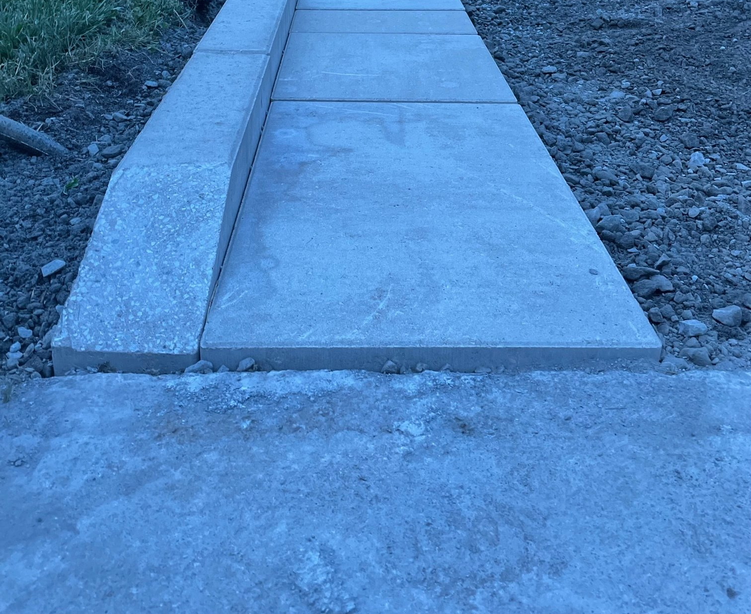 Newly installed concrete sidewalk with a curb and unfinished gravel edge.
