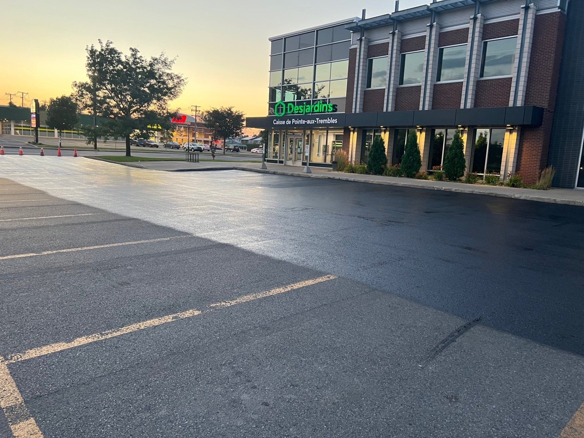 Stationnement nouvellement pavé devant un immeuble commercial avec signalisation verte. Ciel du soir.