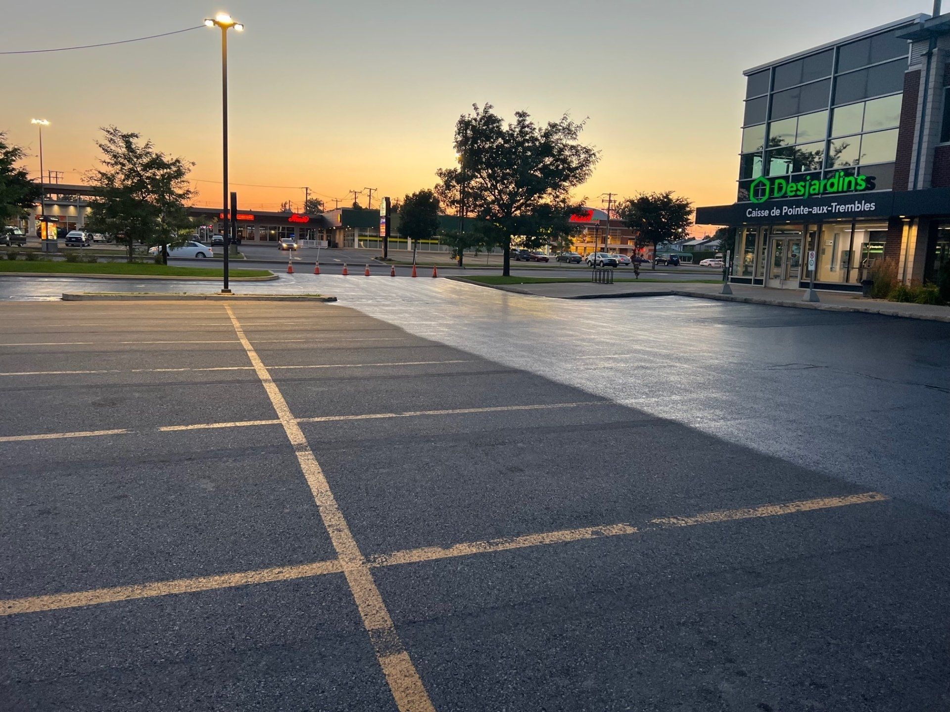 Parking vide au coucher du soleil, avec un bâtiment et une rue en arrière-plan.