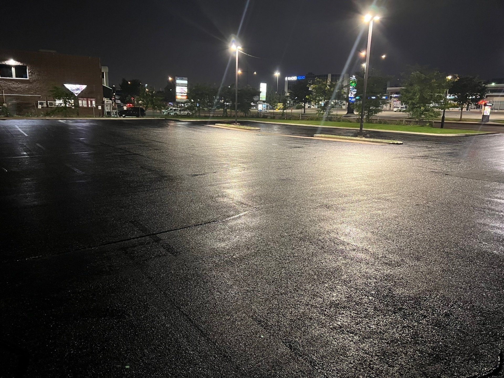 Stationnement en asphalte mouillé reflétant les lampadaires lumineux la nuit.