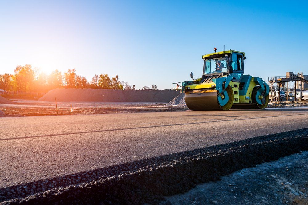 Rouleau compresseur compactant l'asphalte sur un chantier de construction sous un ciel bleu vif.